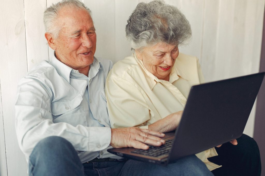 An elderly couple sitting together using a laptop computer.