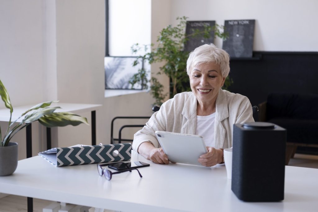 Woman with white and short hair sitting on a chair in front of a white table using and smart home device 